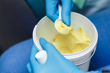 The orthodontist picks up alginate paste with a measuring spoon to take an impression of the patient's teeth.