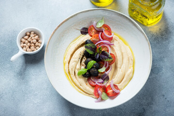 Beige plate with hummus and tomato salad on a light-blue stone background, elevated view, studio shot