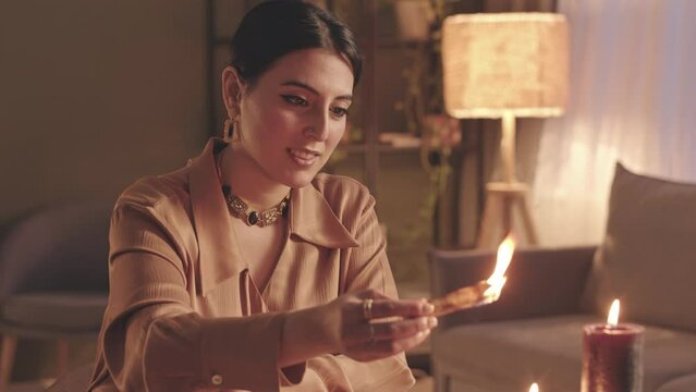 Waist up slowmo of young Middle Eastern fortune teller burning palo santo stick during seance with client