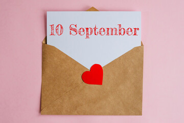 Kraft envelope with a white sheet of paper and a date 10 september, with a red heart. Flat lay on pink background, romance and love concept
