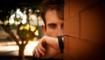 Portrait of man sticking out of a brick wall covering his mouth