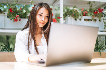 Young asian woman student freelancer with long hair working on laptop in street cafe