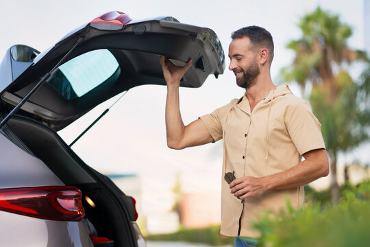 Handsome Smiling Hispanic Man Buying New Car. Successful Bearded Driver Opening Car Trunk Planning Road Trip. Transportation Concept  