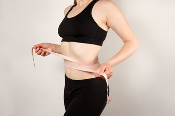 A woman measures the circumference of the abdomen with a centimeter tape, close-up. Slimming concept