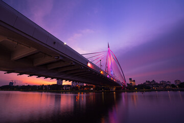 Sunset under the Seri Wawasan Bridge, Putrajaya. Sunbeams and bridge reflecting in water. Colorful sky and alternately illuminated bridge.