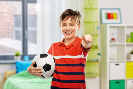 sport, football and leisure games concept - happy smiling boy holding soccer ball and pointing to camera over home room background