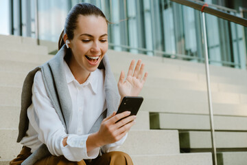 Young woman gesturing and using cellphone while sitting on stair