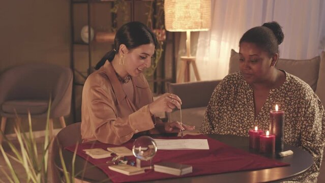 Waist up slowmo of fortune teller using pendulum over astrological and natal chart of client during spiritual seance