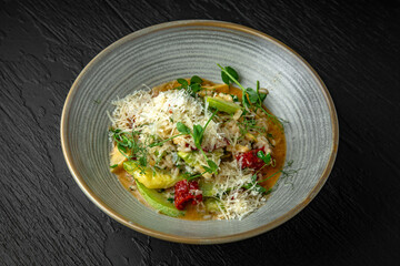 Risotto with artichokes, sun-dried tomatoes and zucchini in a ceramic plate on a dark textured background. Restaurant menu Isolated on black