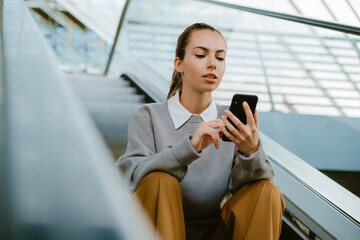 Young woman using mobile phone while sitting escalator's stair