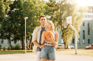 sport, love and people concept - happy young couple with ball on basketball playground