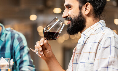 leisure, drinks and people concept - close up of happy man with glass drinking red wine at restaurant
