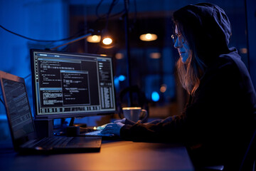 cybercrime, hacking and technology concept - female hacker in dark room writing code or using...