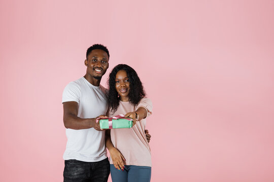 Cheerful beautiful african american couple showing their gift over pink studio background. African lovers exchanging gifts while anniversary celebration.