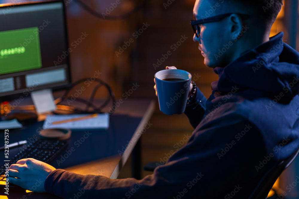 Poster cybercrime, hacking and technology concept - close up of male hacker in dark room drinking coffee an