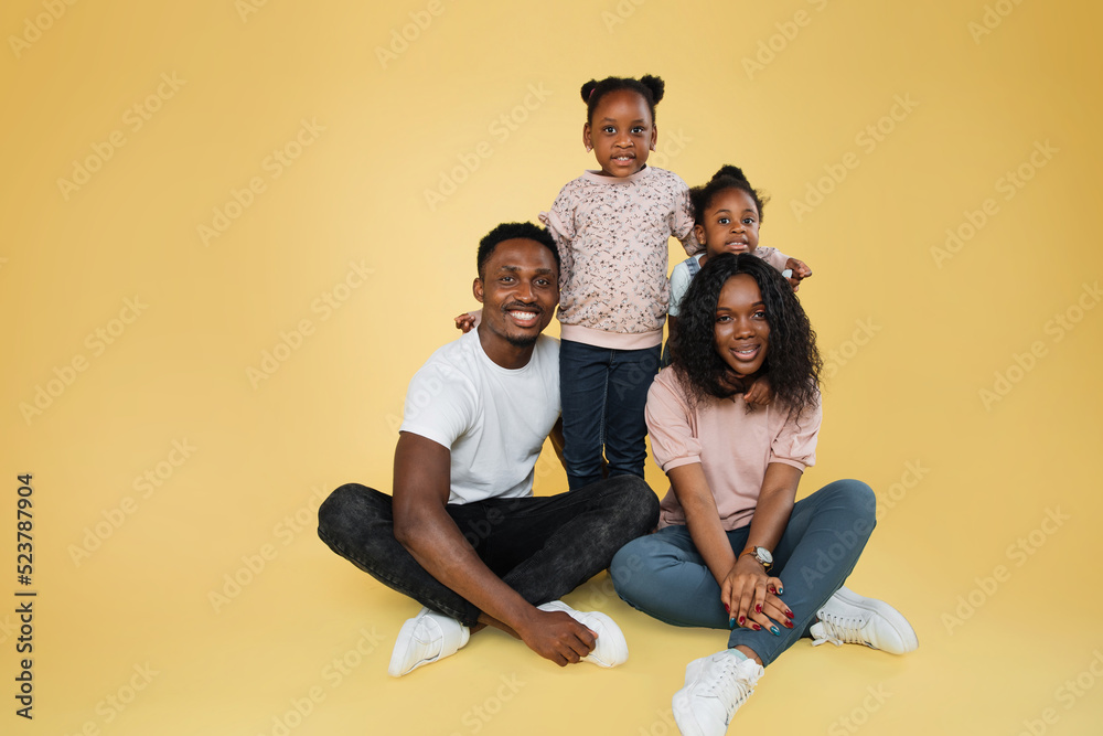 Wall mural happy family concept. young parents hugging sitting down on the floor while their daughters standing