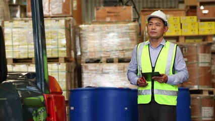 warehouse manager. Warehouse manager and staff driving forklift operator moving boxes in industrial container warehouse factory. Asian senior Man worker woking with forklift.