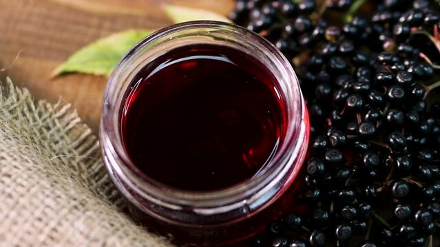 Close-up Natural elderberry juice in a glass jar. Black elderberry on a wooden background. Herbal medicine. Homeopathy, black berry on an old table