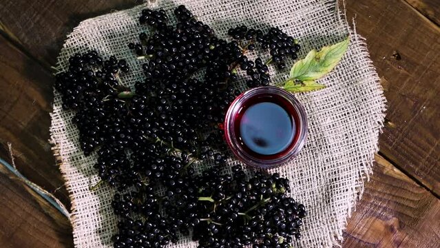 Top view on a turntable Natural elderberry juice in a glass jar. Black elderberry on a wooden background. Herbal medicine. Homeopathy, black berry on an old table