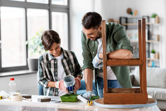 repair, diy and home improvement concept - happy smiling father and son in protective gloves pouring grey color paint into tray for painting old wooden table