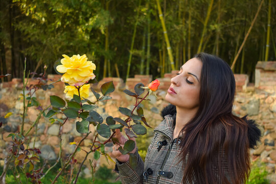 Chica joven con el pelo largo, oliendo las rosas de un jardín