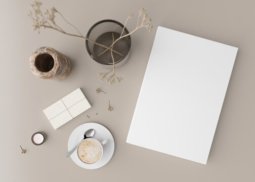White book cover mock up with coffee cup, vase and other home accessories on beige table. Blank template for your design. Top view, close-up. Book, catalogue or magazine cover presentation. 3D render.