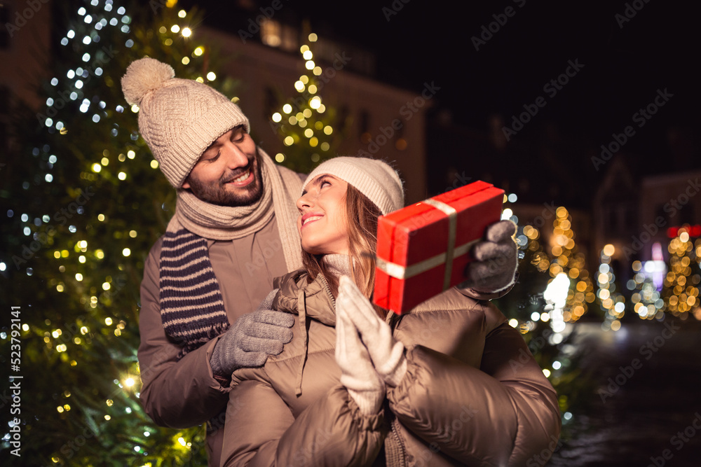 Canvas Prints winter holidays and people concept - happy smiling couple with gift over christmas tree lights in ev