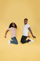 Fototapeta na wymiar Full length shot of jumping african couple having fun together. Studio photo of young people on yellow background, copy space