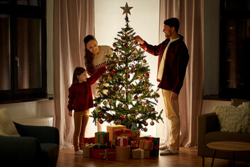 family, winter holidays and people concept - happy mother, father and little daughter decorating christmas tree at home