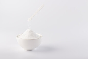 A small spoon pours the sugar substitute into the bowl.
Vertical photo of a sugar substitute on a white background in a white bowl. Stevia.