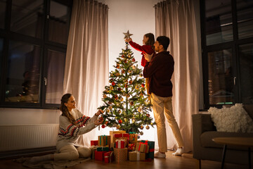 family, winter holidays and people concept - happy mother, father and little daughter decorating christmas tree at home - Powered by Adobe