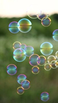 A dark-haired girl enjoys a sunny day while blowing colorful soap bubbles into the air. The bubbles catch the light, creating a playful and whimsical scene