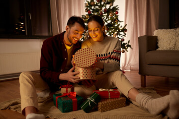 holidays, celebration and people concept - happy couple opening christmas gift box with magical light inside at home