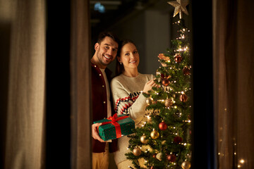 winter holidays and people concept - happy couple with gift box decorating christmas tree at home