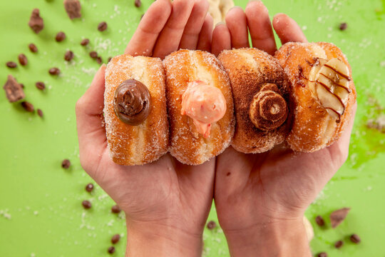 Two hand palms holding stacked four different bombolone doughnuts.