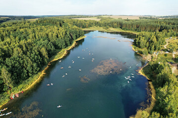 Aerial view of blue forest wild lake with people on floating sup boards. Top view from drone
