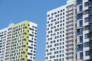 Fototapeta premium Facade of modern building in city. From below of contemporary high rise buildings with glass mirrored windows against cloudless blue sky.