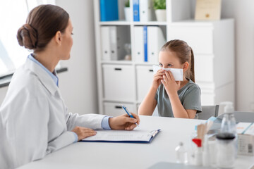 medicine, healthcare and pediatry concept - female doctor or pediatrician and little girl patient blowing her nose on medical exam at clinic