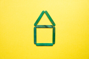 a house made of green wooden sticks on a yellow background in the center.