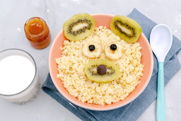 Funny cute kids childrens baby's healthy breakfast lunch oatmeal porridge in bowl look like bear,mouse face decorated with kiwi, banana, dried berry fruits,milk,honey. dessert food art on gray table