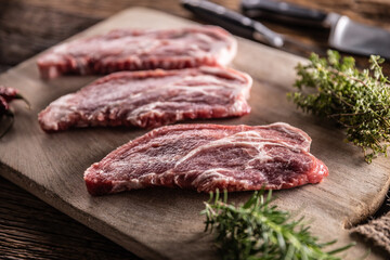 Raw pork neck cut on a cutting board with rosemary and thyme herbs