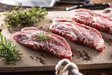 Raw pork neck cut on a cutting board with rosemary and thyme herbs