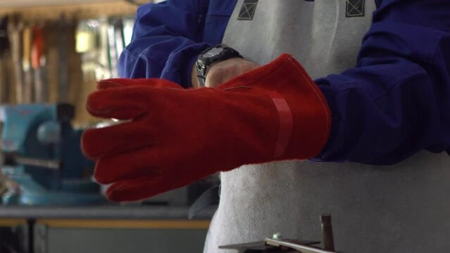 Slowmotion of a man welder putting red gloves for protect the hands. Worker wearing a special clothes works as welding machine in his workshop, safety concept.