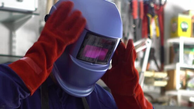 Slowmotion of man welder putting helmet for protect the eyes. Worker wearing a special clothes works as welding machine in his workshop, safety concept.