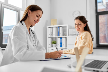 medicine, healthcare and people concept - female doctor with clipboard talking to smiling woman...