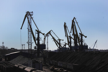 Fototapeta na wymiar silhouettes of cranes on mountains of coal in Port or logistics hub