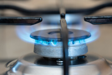 Close-up of a gas stove with gas pouring out and burning. The oven is on. The flame glows blue.