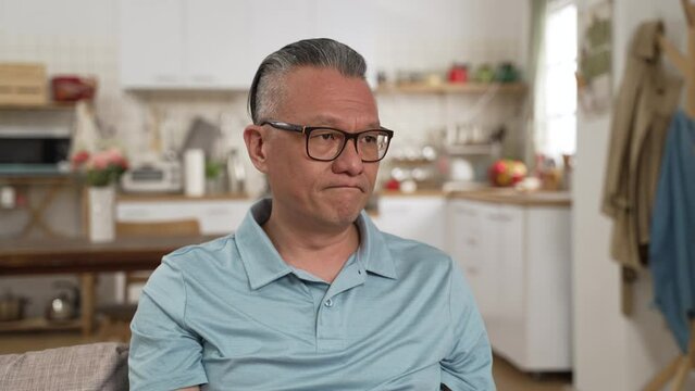 worried Japanese mature man having headache while considering hard decision alone at home. he stares into distance and shakes head feeling stressed out