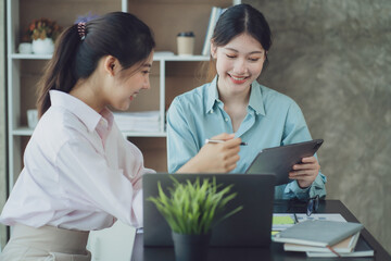 Smiling young Asian businesswomen talking to colleague and exchanging ideas together at office.