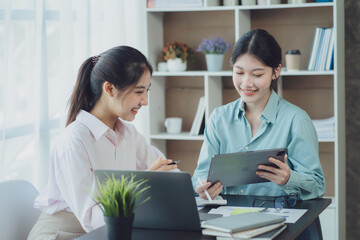 Smiling young Asian businesswomen talking to colleague and exchanging ideas together at office.